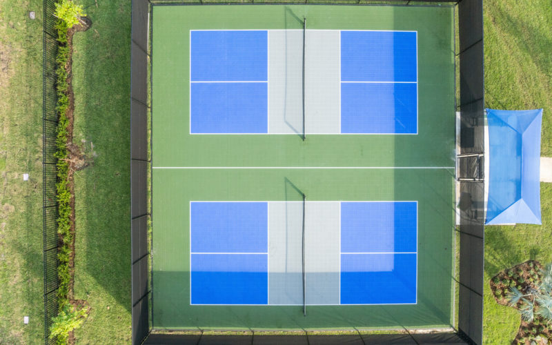 Aerial view of the pickleball courts at Aviva Port St. Lucie, showcasing well-maintained playing surfaces and nearby shaded seating.