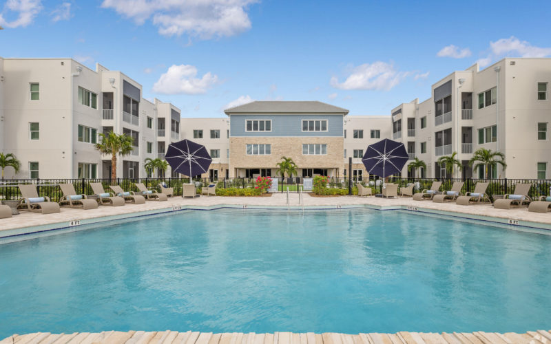 Resort-style pool at Aviva Port St. Lucie with spacious lounging areas, umbrellas, and landscaped surroundings.